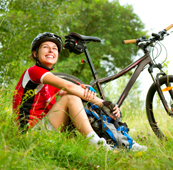 Girl wearing a bike helmet sitting in the grass near a bike looking up at the sky