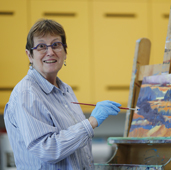 Older adult holding paint brush in front of a partially painted canvas
