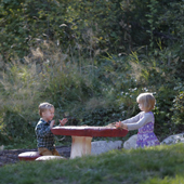 Two young children sitting outdoors at a table in a park 